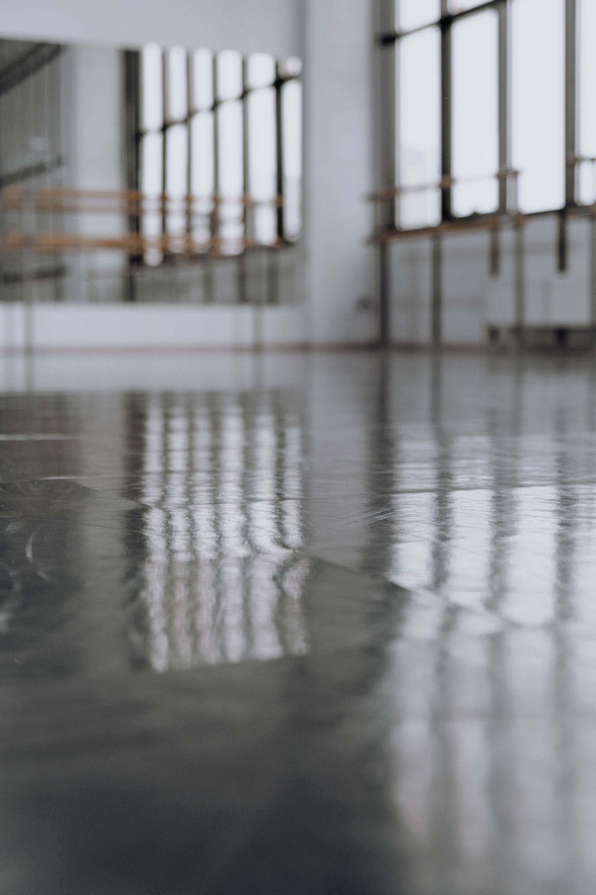Floor reflection capturing sleek modern dance studio with mirrors and large windows.